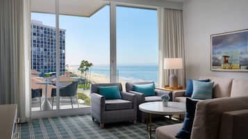 Una habitación de hotel con un ventanal grande, un balcón, un sofá, una mesita de café y un cuadro en la pared.