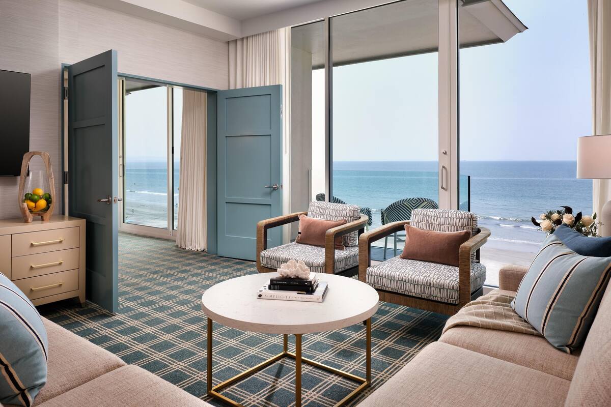 Une chambre d’hôtel dotée d’une grande fenêtre, d’un canapé, de deux fauteuils, d’une table basse et d’un téléviseur.
