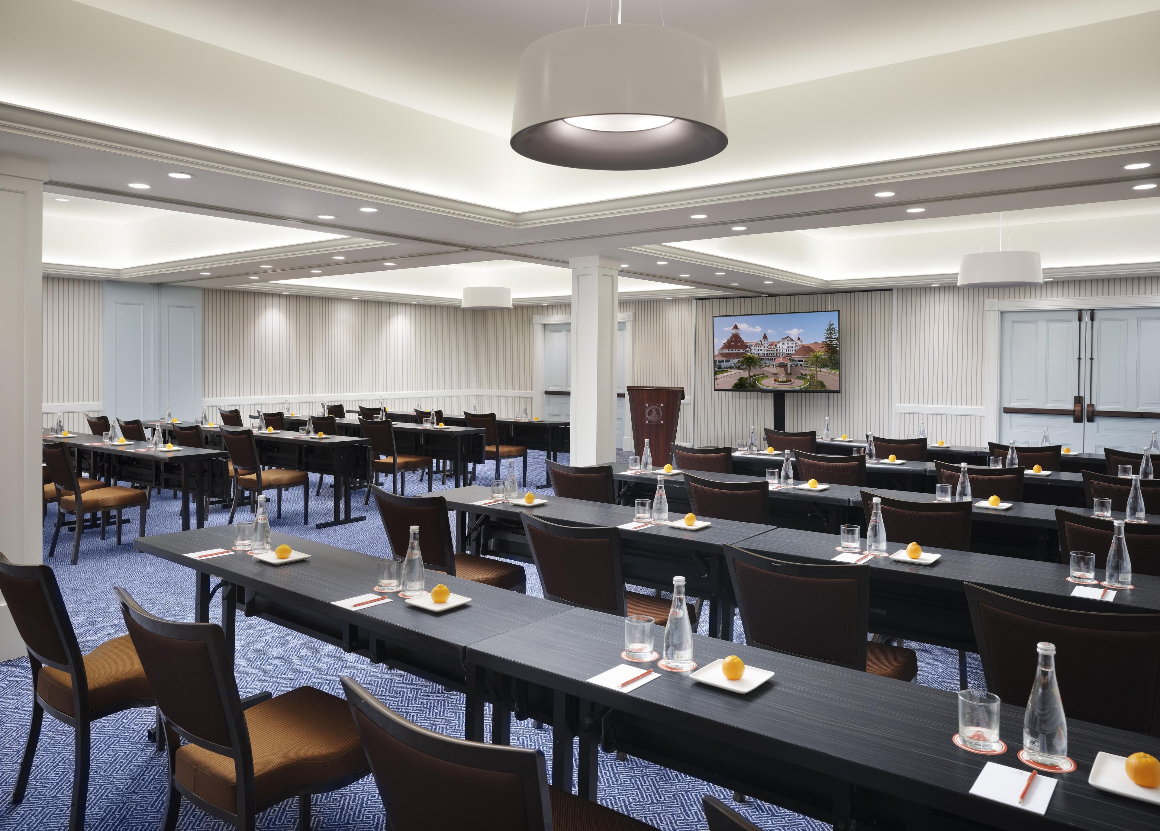 A conference room with multiple tables, chairs, and a television screen on the wall.