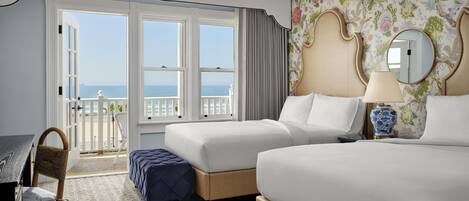 Habitación de hotel con dos camas, un escritorio, una silla y un balcón con vista al mar.
