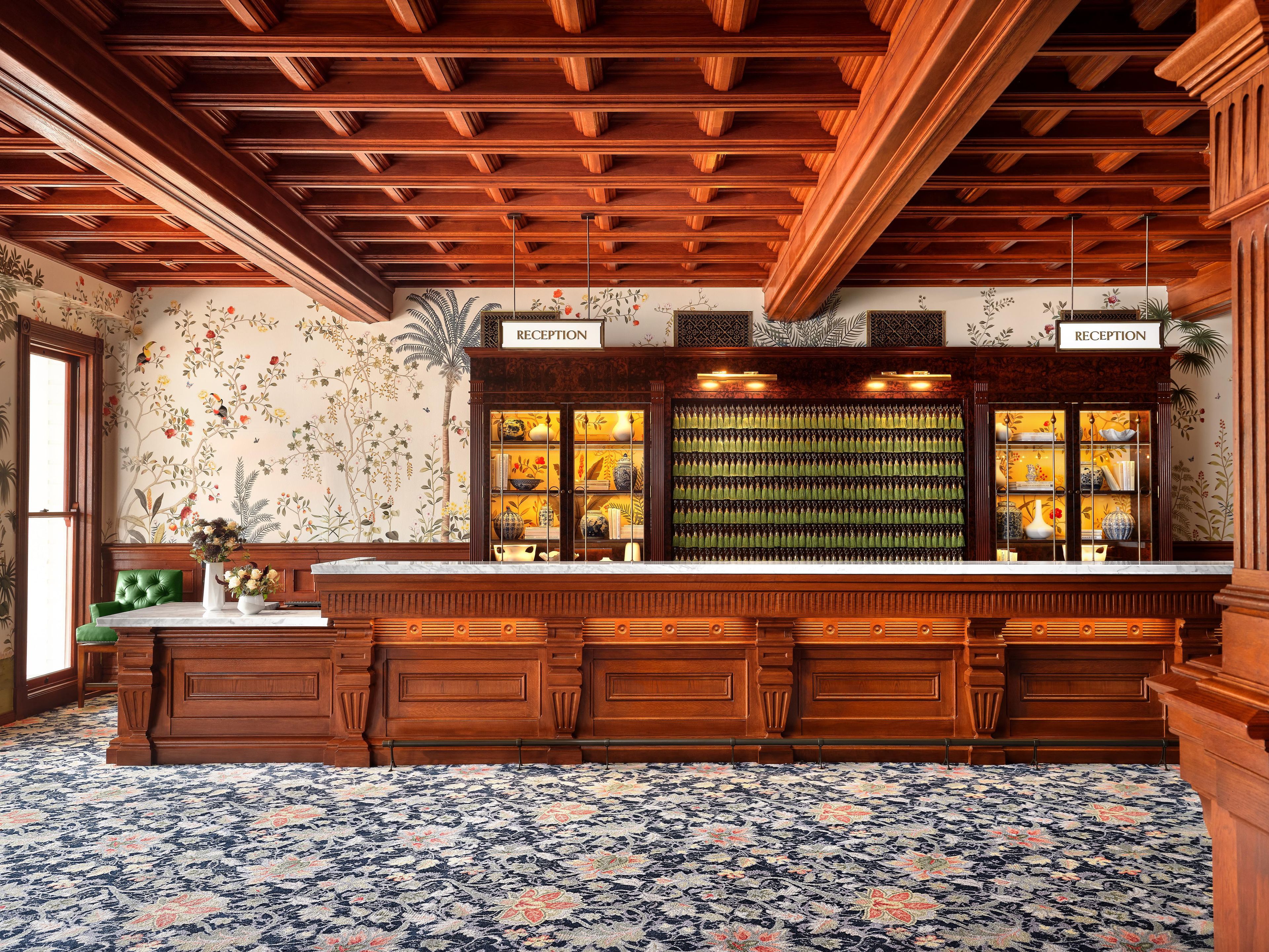 A reception area with a wooden reception desk, a floral patterned carpet, and a wall with a floral wallpaper design.