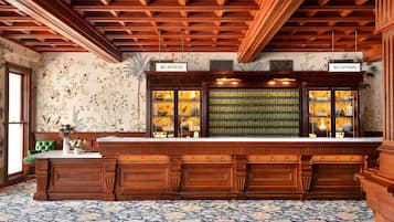 A reception area with a wooden reception desk, a floral patterned carpet, and a wall with a floral wallpaper design.