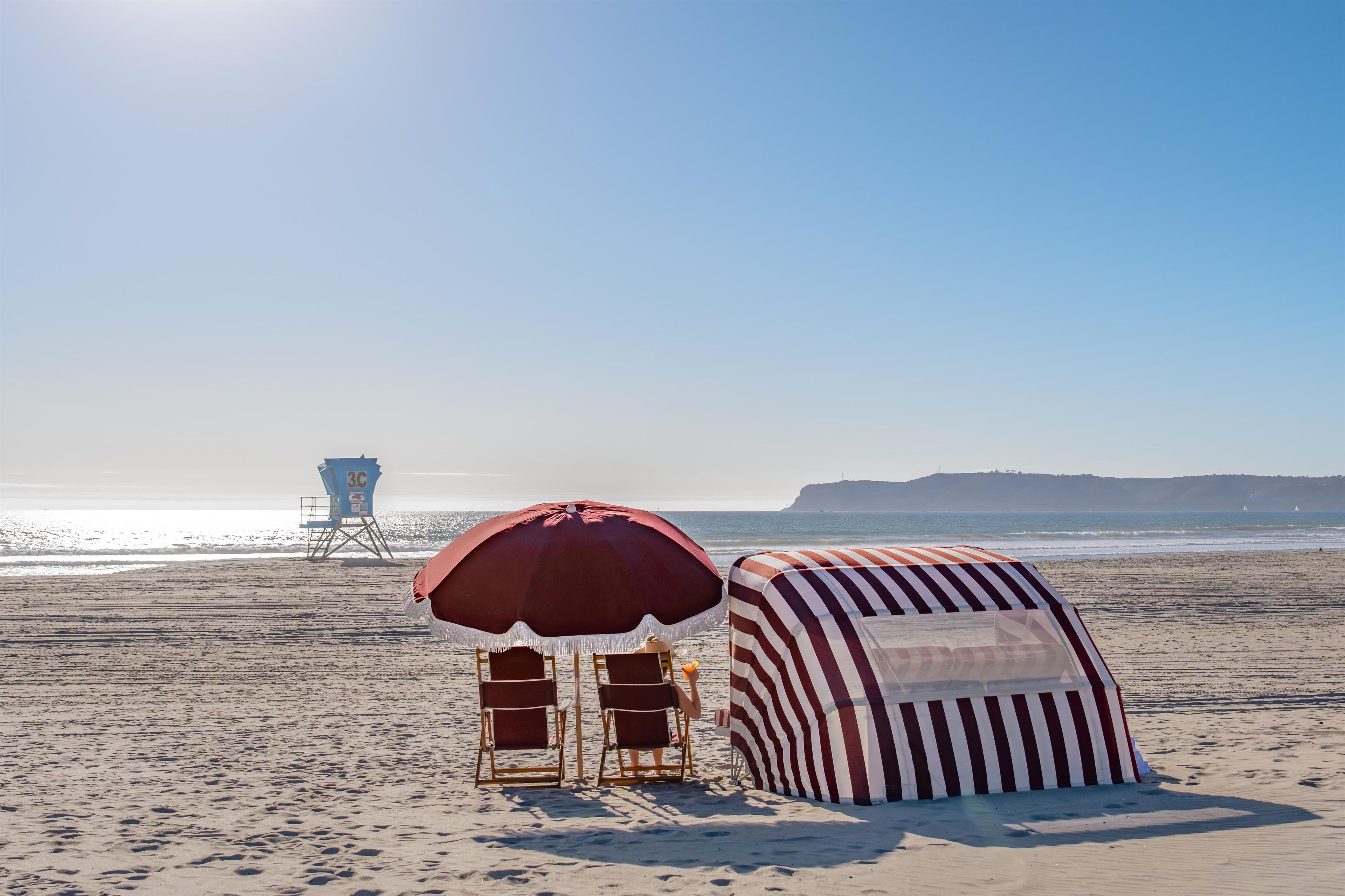 A beach with a lifeguard tower, striped beach umbrellas, and beach chairs.