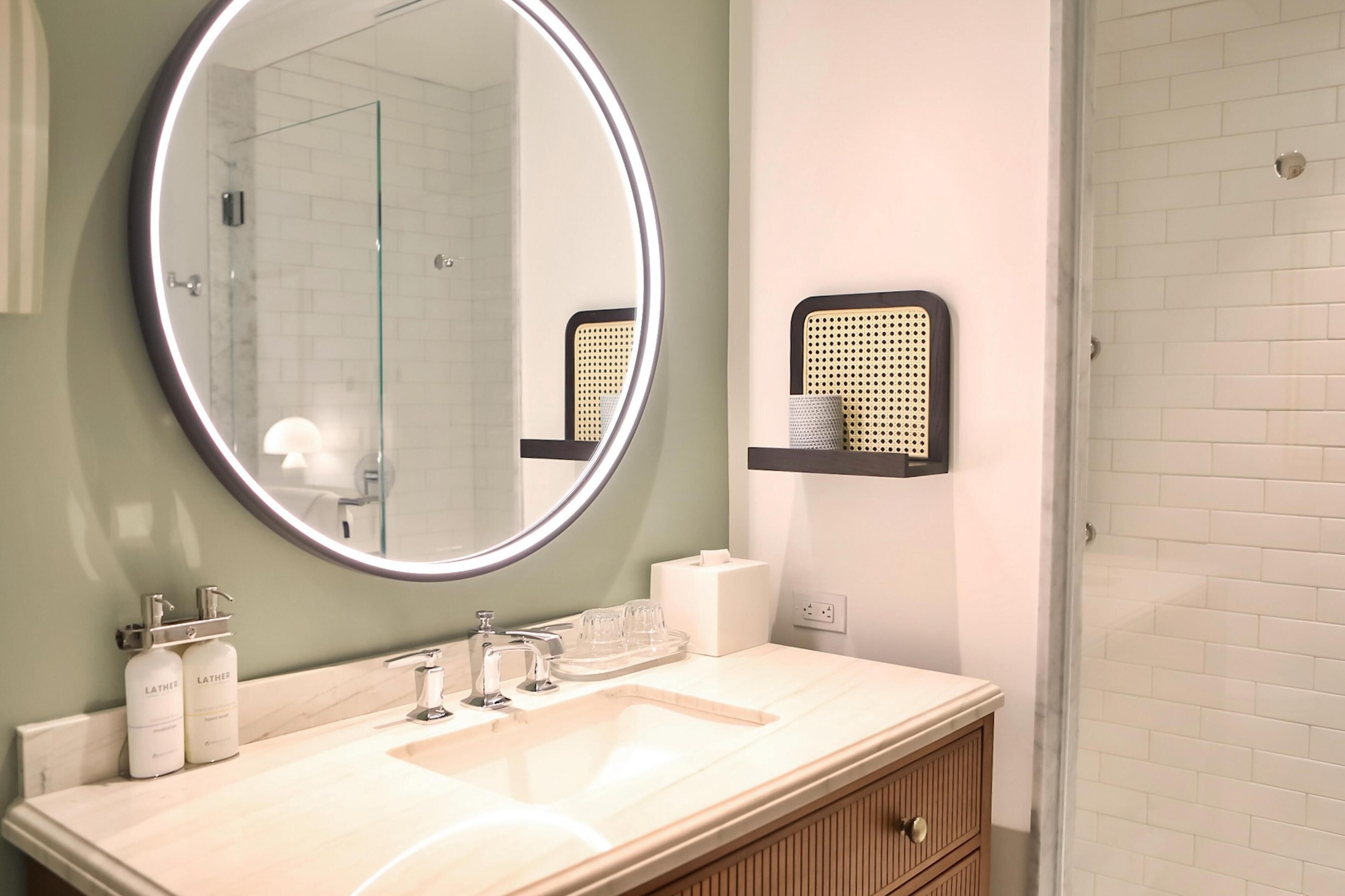 A bathroom with a round mirror, a sink, a towel rack, and a shower.