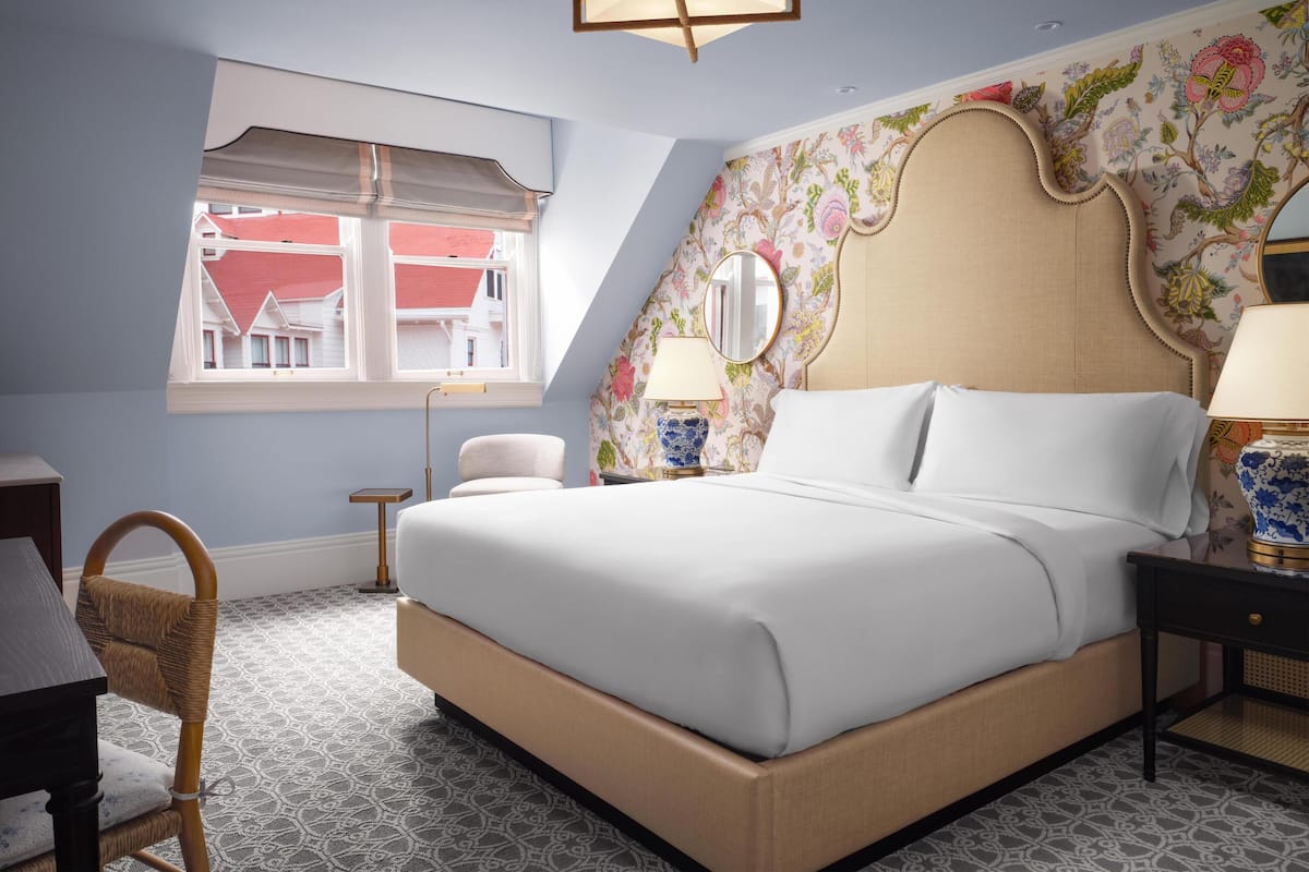Une chambre avec un grand lit, une fenêtre donnant sur des immeubles, une chaise et une table de chevet avec une lampe.