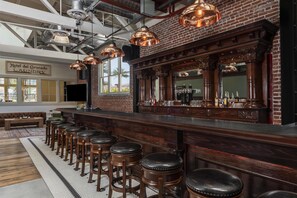 A bar area with a brick wall, wooden bar counter, and multiple stools.