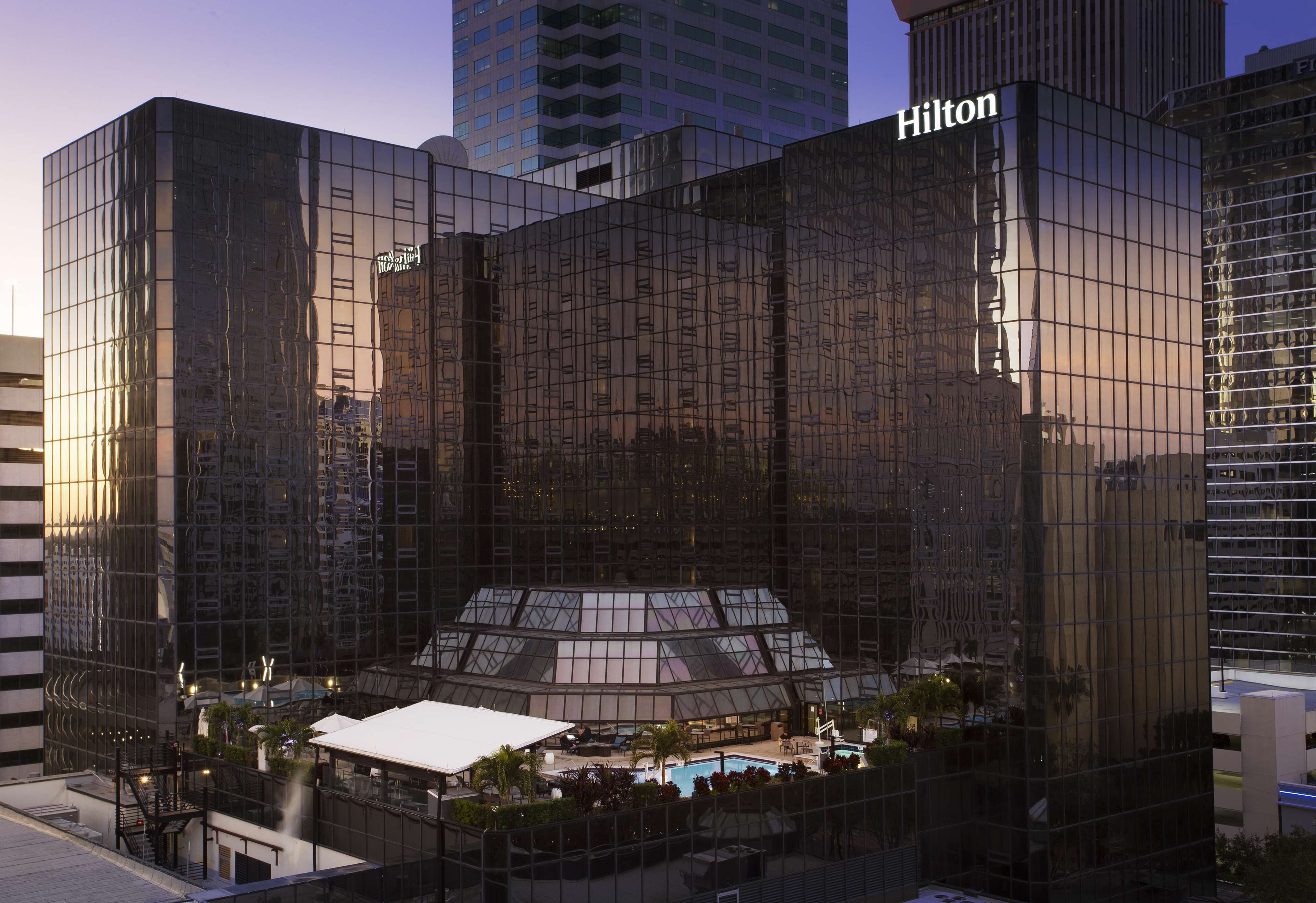 A modern hotel with a glass facade, a rooftop pool, and a prominent Hilton sign.