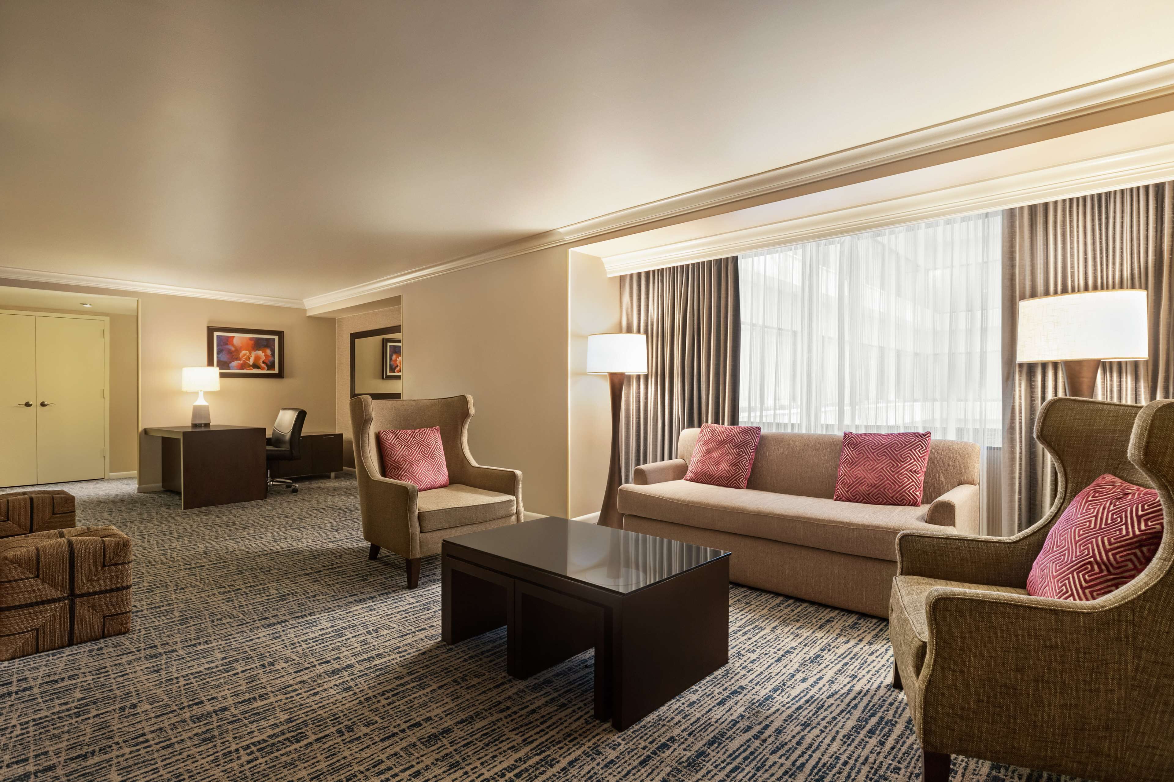 Una habitación de hotel con sofá, sillones, una mesa de centro, un escritorio y una lámpara.