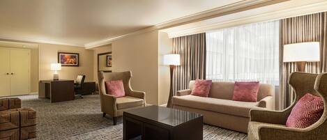 Una habitación de hotel con sofá, sillones, una mesa de centro, un escritorio y una lámpara.