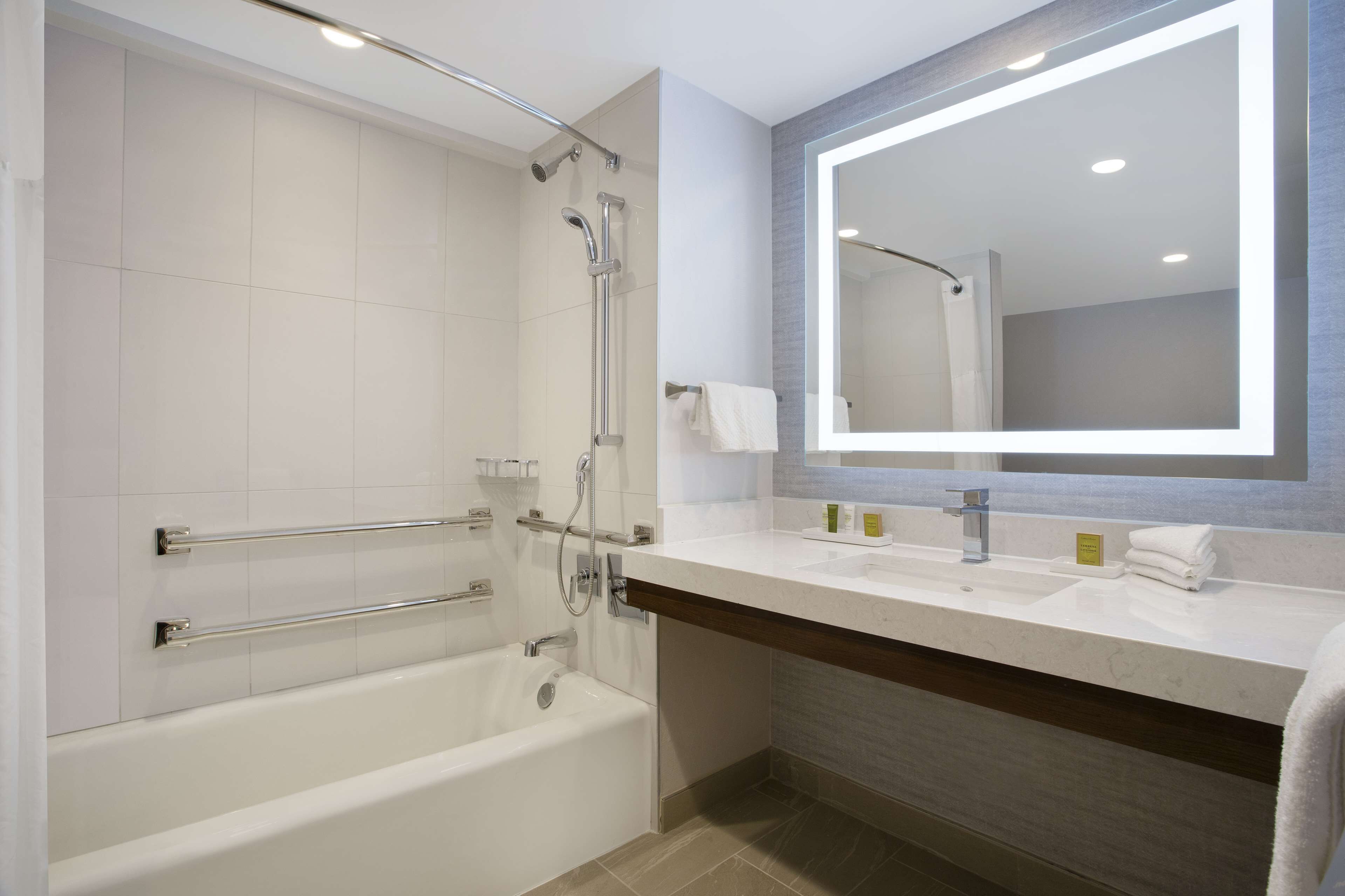 A modern bathroom with a bathtub, a shower with a glass door, a large mirror, and a vanity with a sink and towel rack.