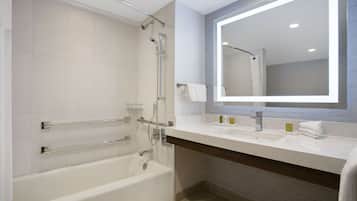 A modern bathroom with a bathtub, a shower with a glass door, a large mirror, and a vanity with a sink and towel rack.