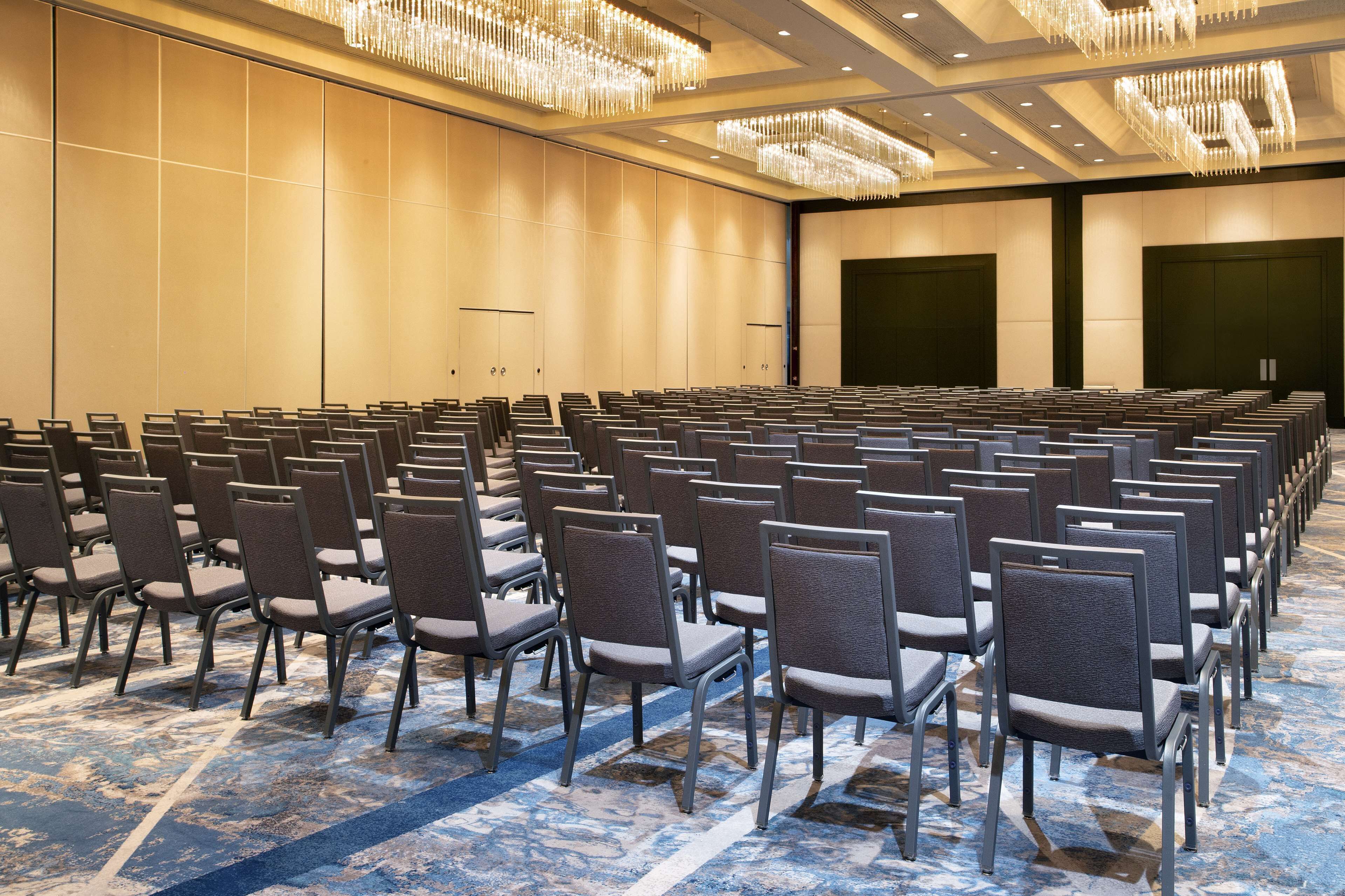Un salón de conferencias con filas de sillas, una alfombra estampada y una gran araña de cristal.