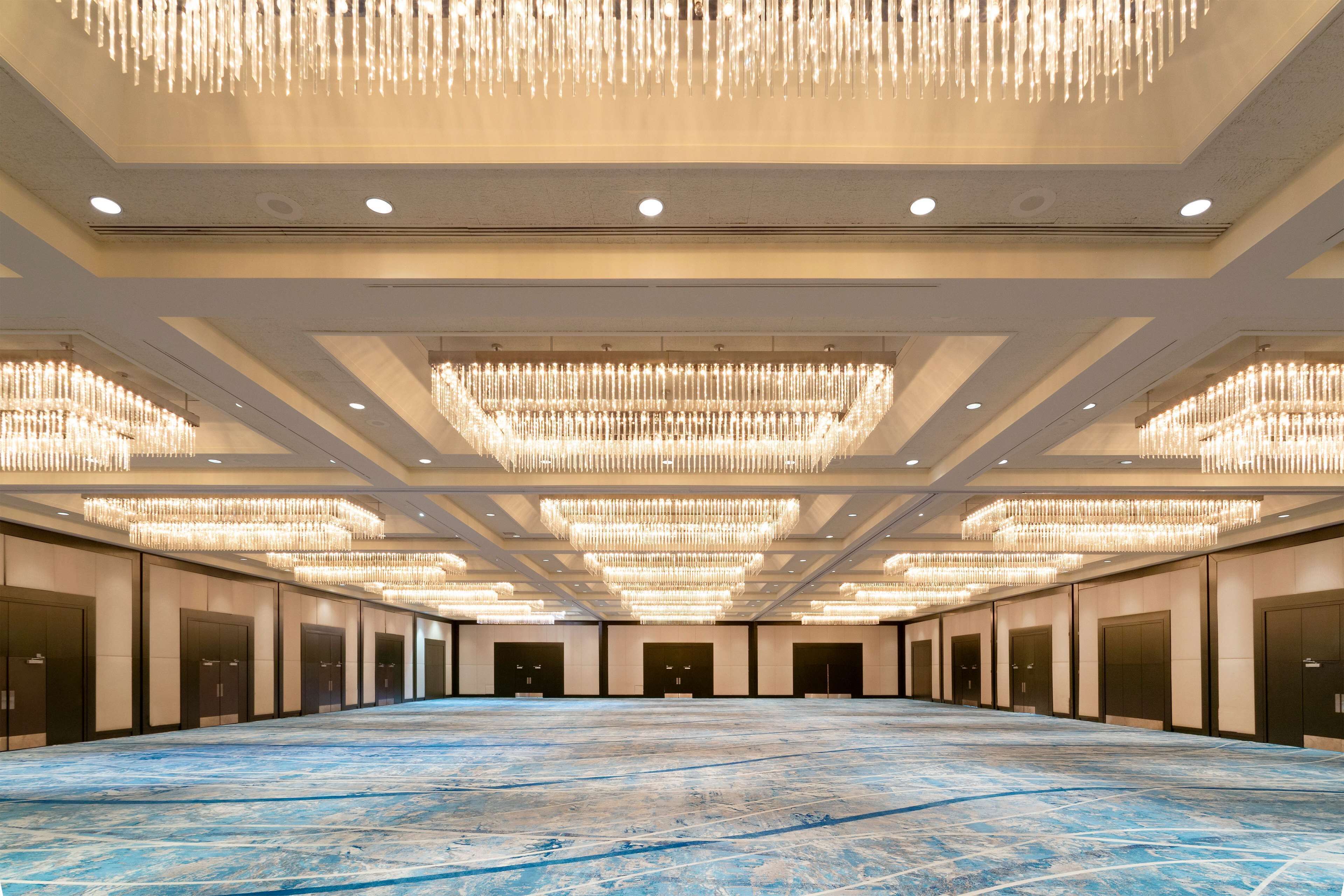 A spacious hall with a blue marble floor, multiple chandeliers, and a row of doors on one side.
