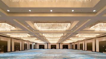 A spacious hall with a blue marble floor, multiple chandeliers, and a row of doors on one side.