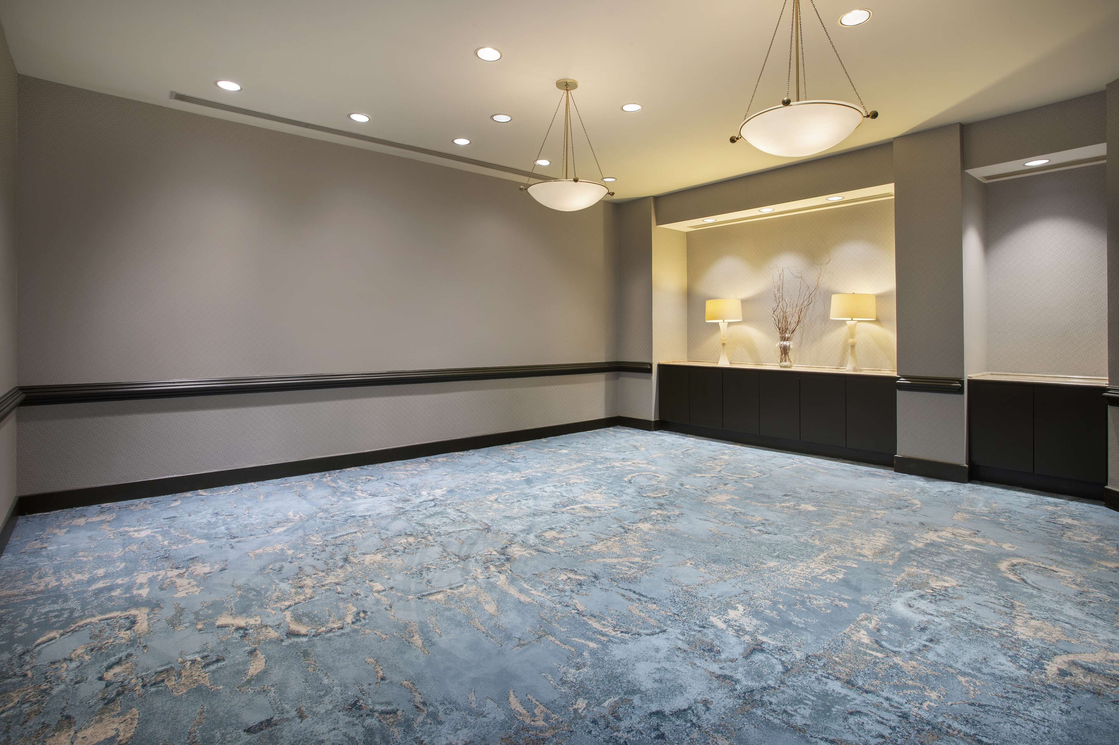 Um quarto espaçoso com piso de mármore azul, iluminação embutida no teto e um espelho fixado na parede com duas luminárias.
