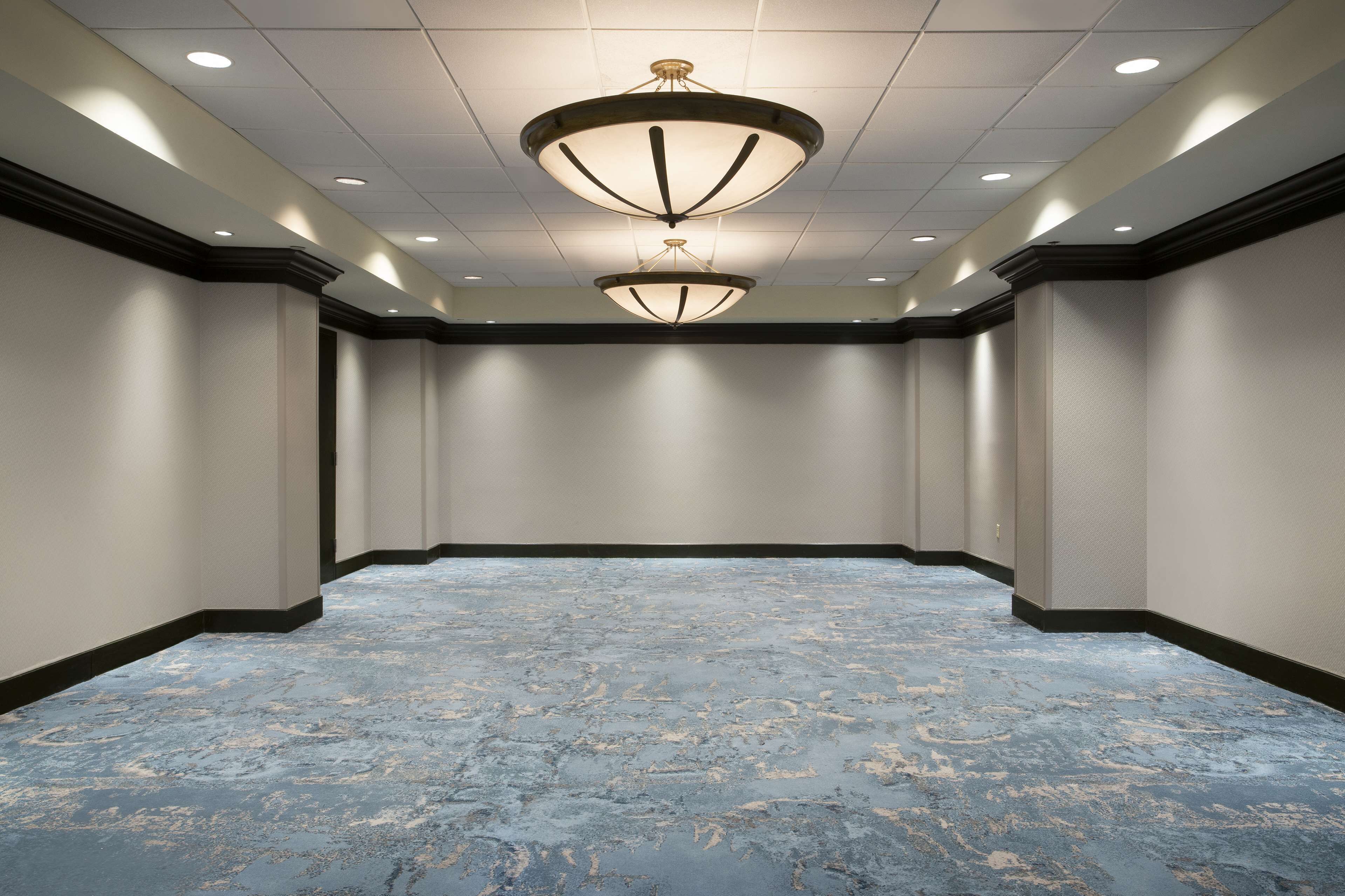 Una sala de conferencias con alfombra de diseño azul, iluminación empotrada en el techo y un diseño de pared simétrico.
