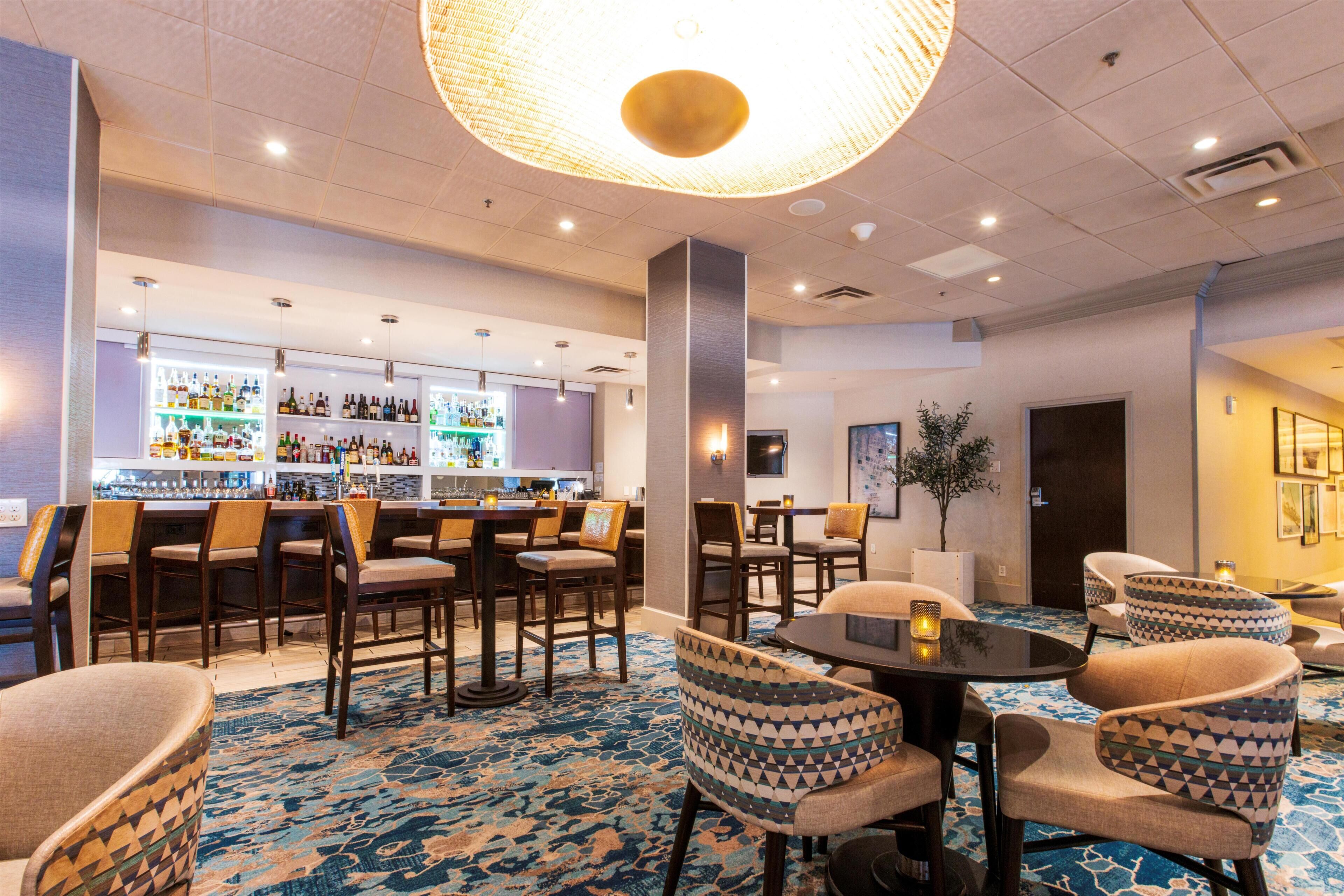 Un vestíbulo de hotel con zona de bar, arreglos de asientos y una lámpara decorativa en el techo.