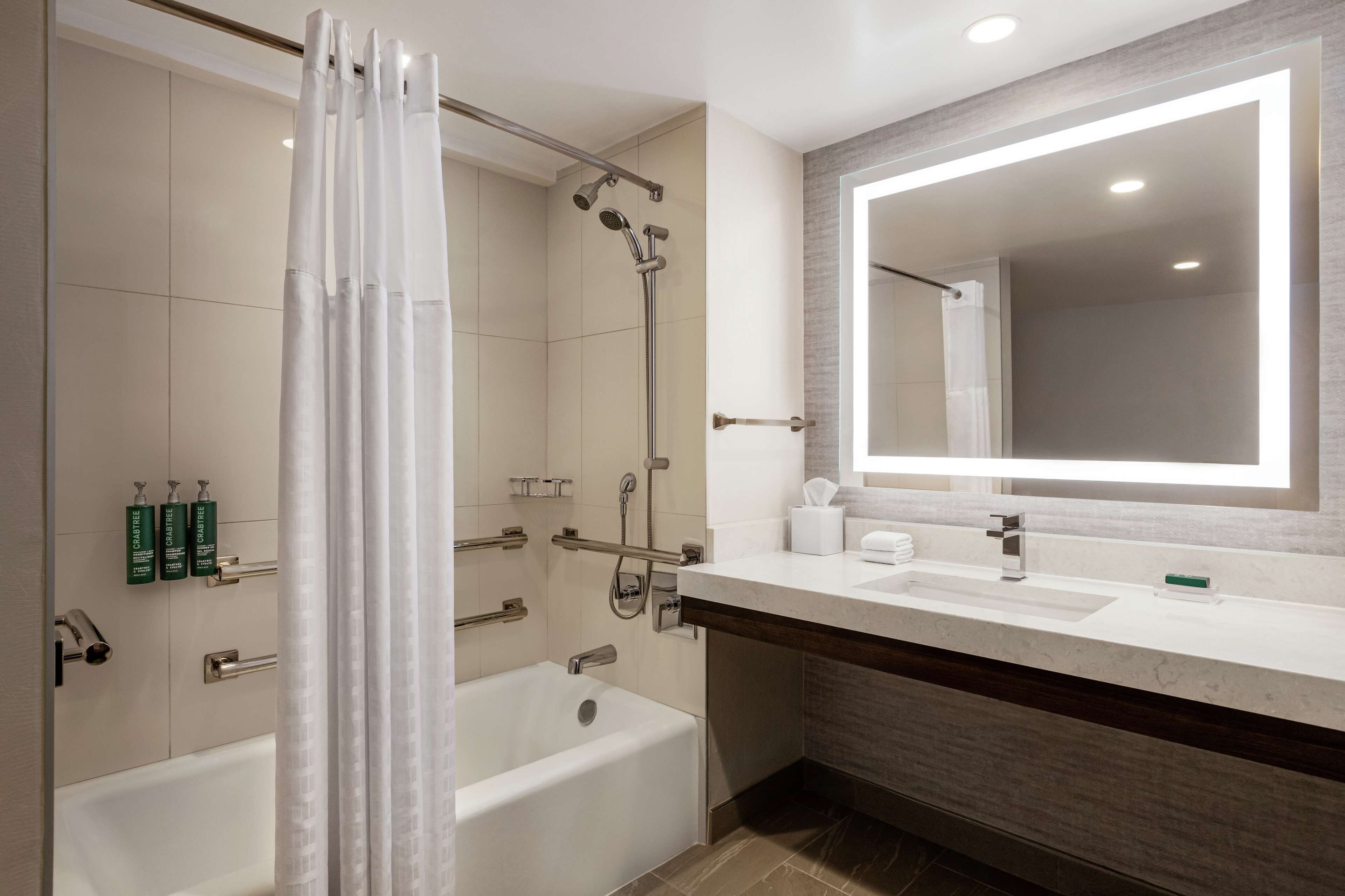 A modern bathroom with a bathtub, shower, and a large mirror above the sink.