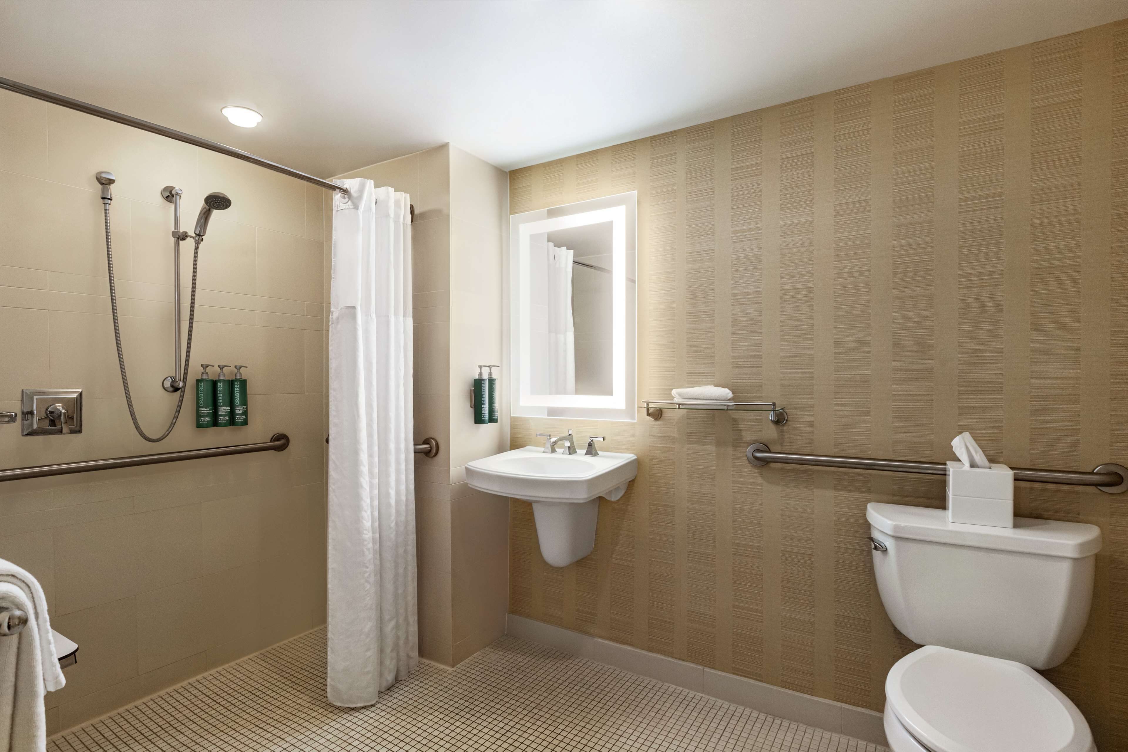 A bathroom with a shower, sink, and toilet, featuring a tiled floor and a mirror above the sink.