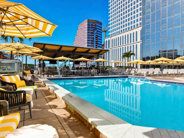 A swimming pool with lounge chairs and umbrellas, surrounded by high-rise buildings. - Hilton Tampa Downtown (Tampa)