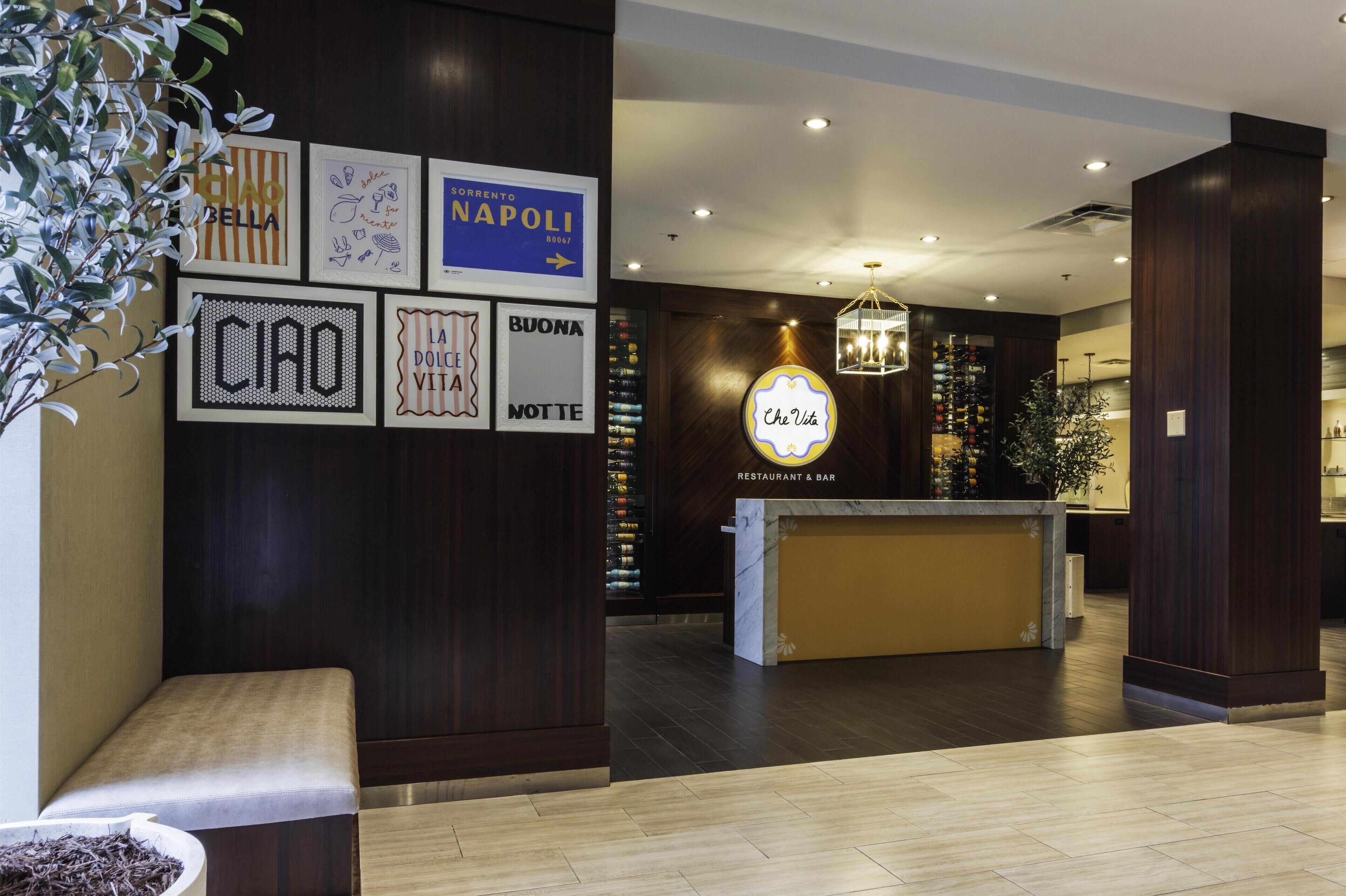 A hotel lobby with a reception desk, framed pictures on the wall, and a potted plant.