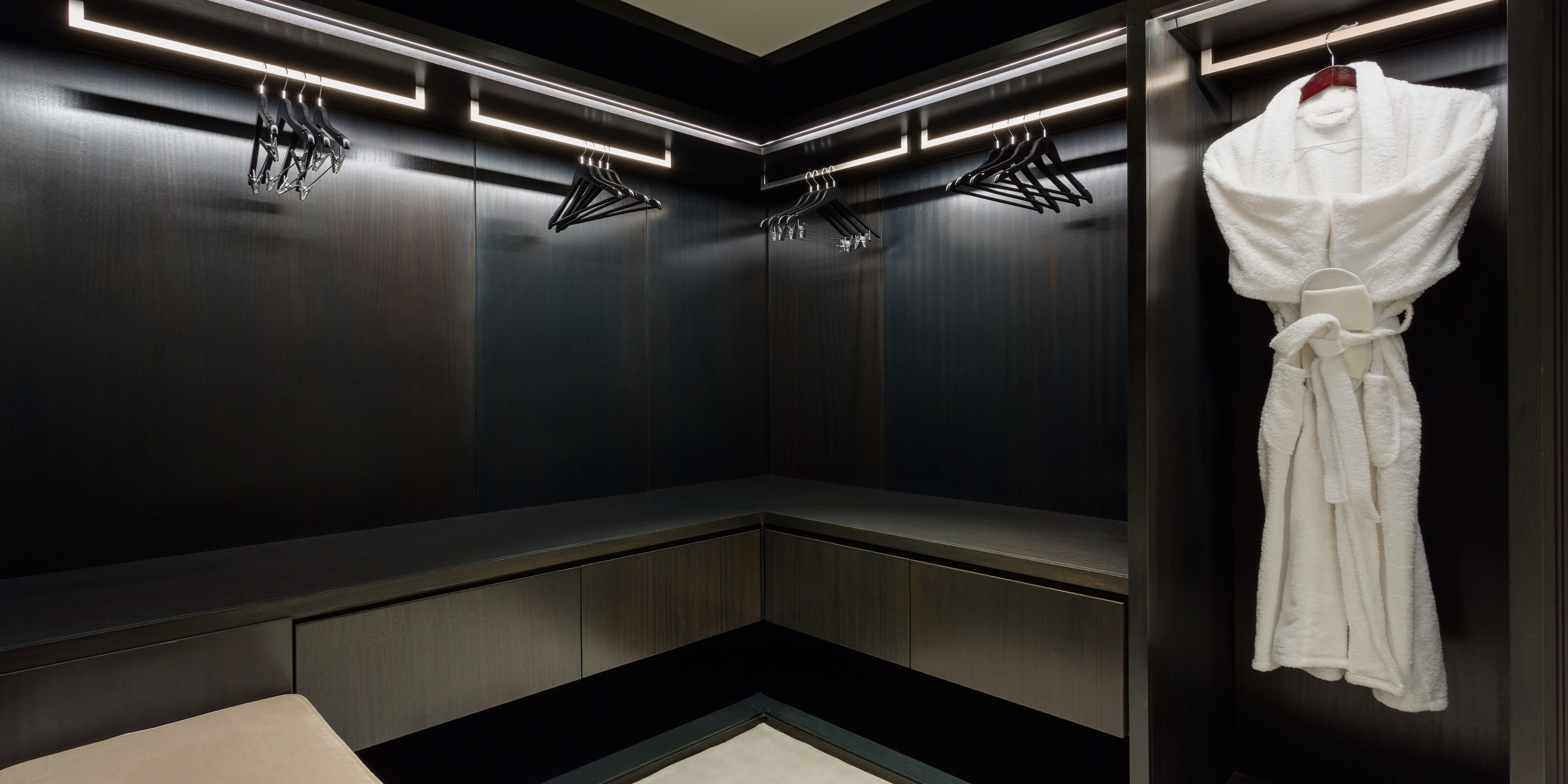 A modern, dimly lit walk-in closet with dark wood paneling, a bench, and a hanging robe.