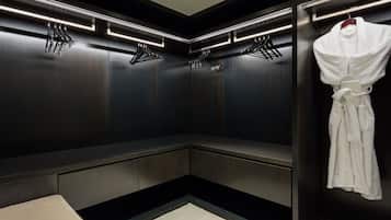 A modern, dimly lit walk-in closet with dark wood paneling, a bench, and a hanging robe.