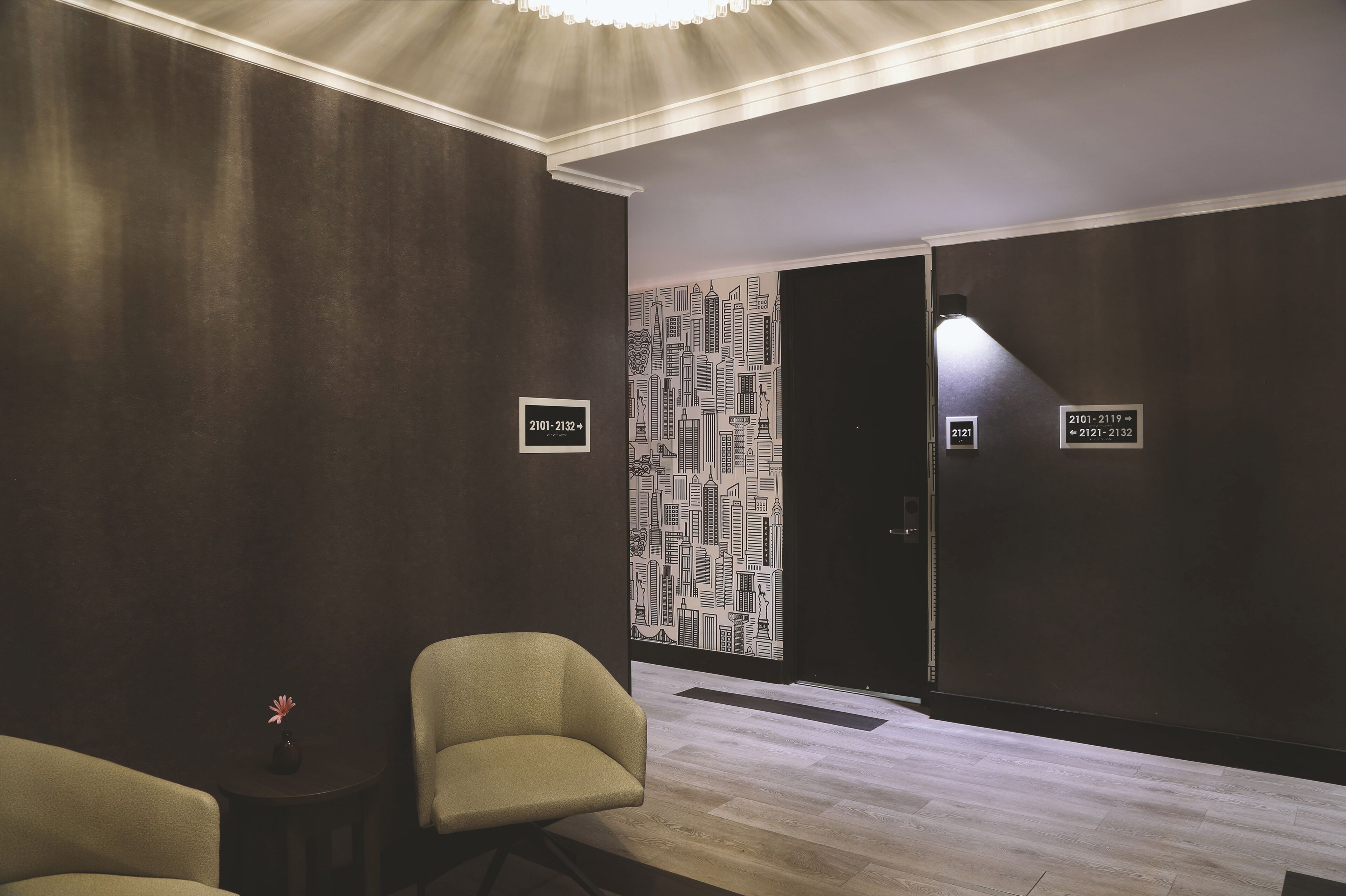 A hotel lobby with a modern design, featuring a cityscape wall, a reception desk, and seating areas.