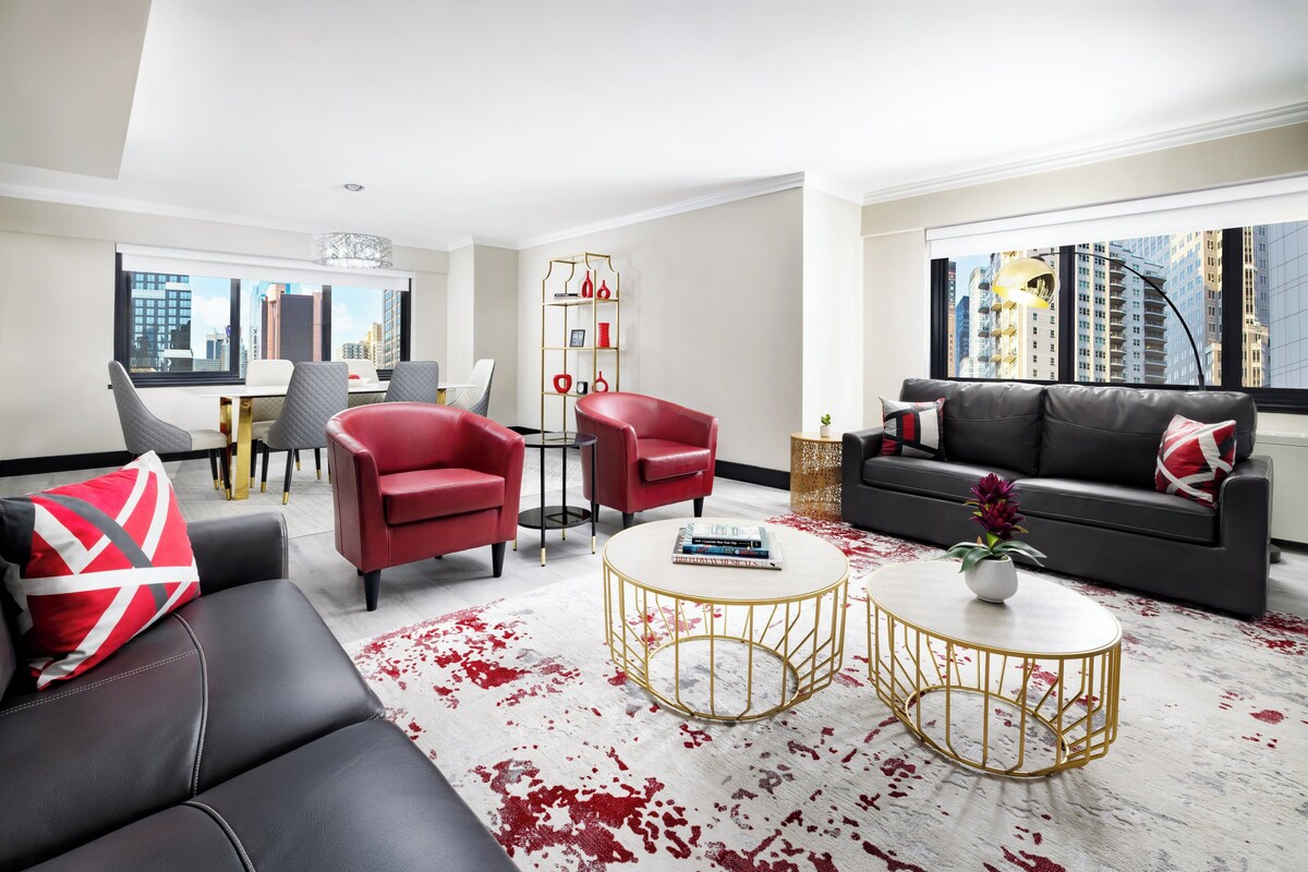 Una sala de estar moderna con un sofá de cuero negro, sillones rojos y una mesa de centro blanca.