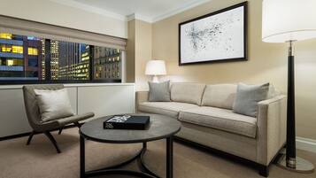 A hotel room with a sofa, armchair, round coffee table, and a lamp.