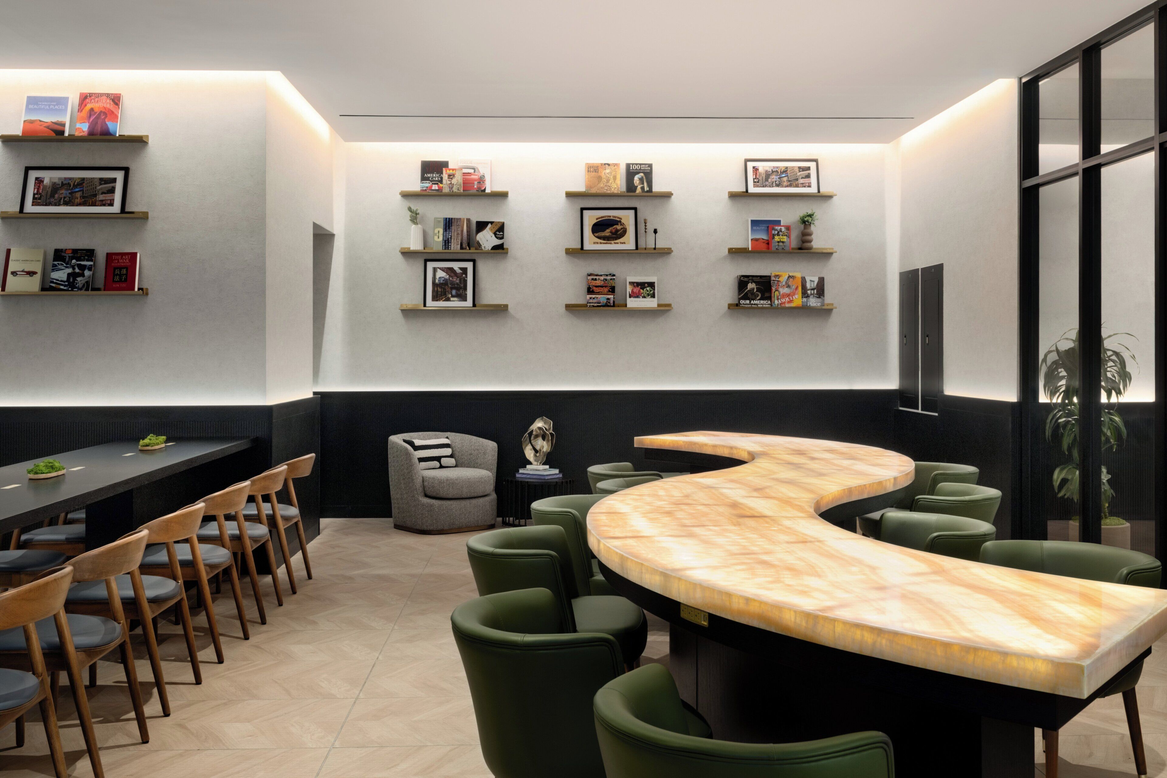 Een moderne vergaderruimte met een gebogen marmeren tafel, groene stoelen met bekleding en boekenkasten met ingelijste foto’s aan de wanden.