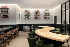 Une salle de conférence moderne, dotée d’une table en marbre aux lignes courbes, de chaises recouvertes d’un tissu vert et d’étagères remplies de livres, avec des tableaux encadrés accrochés aux murs.