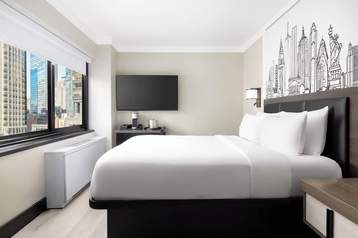 Un moderno cuarto de hotel con una cama grande, un televisor de pantalla plana, un mural de un paisaje urbano y vistas de edificios altos.