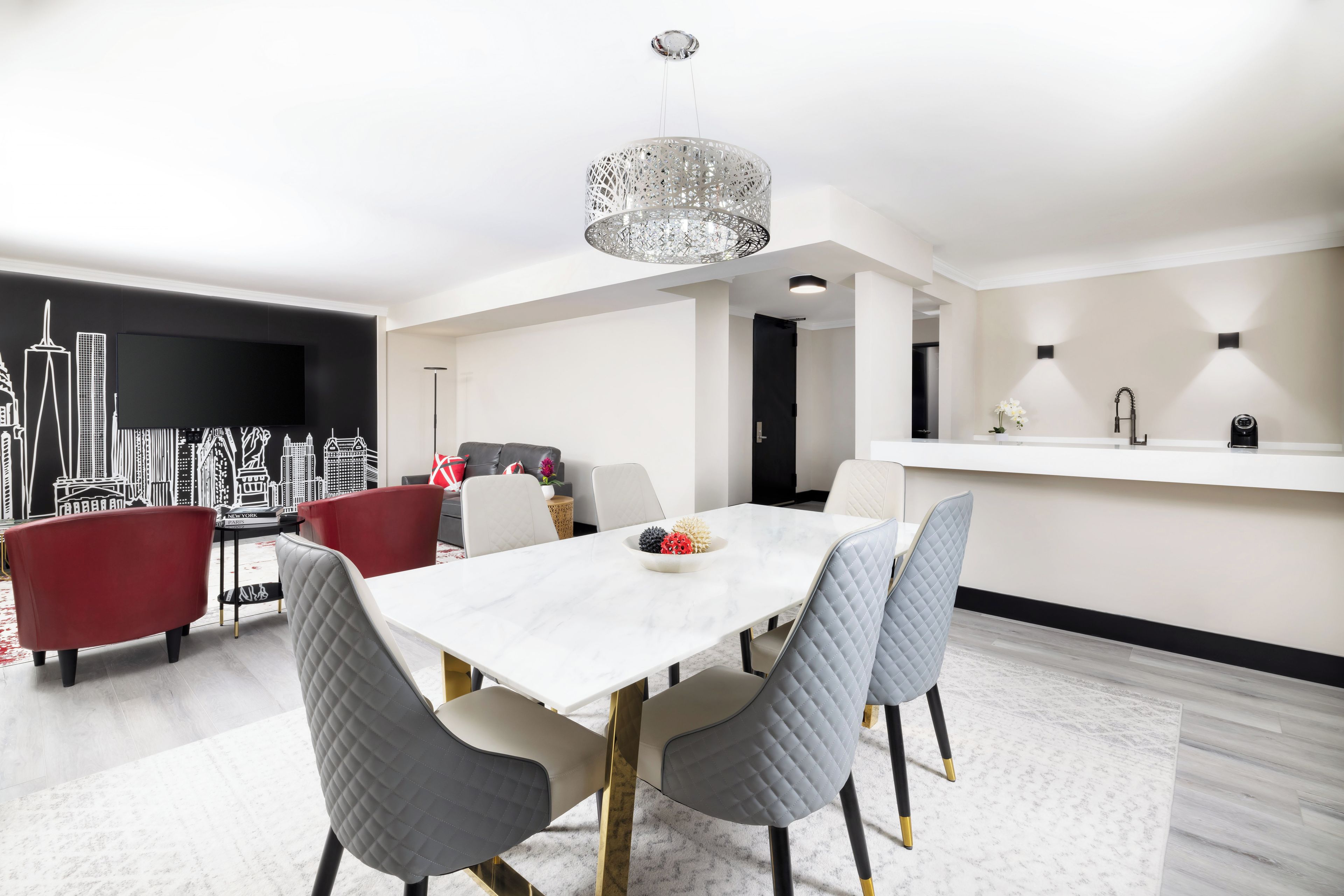A modern dining area with a white table, grey upholstered chairs, and a decorative chandelier.