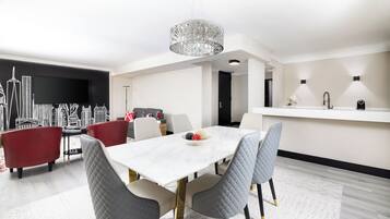A modern dining area with a white table, grey upholstered chairs, and a decorative chandelier.