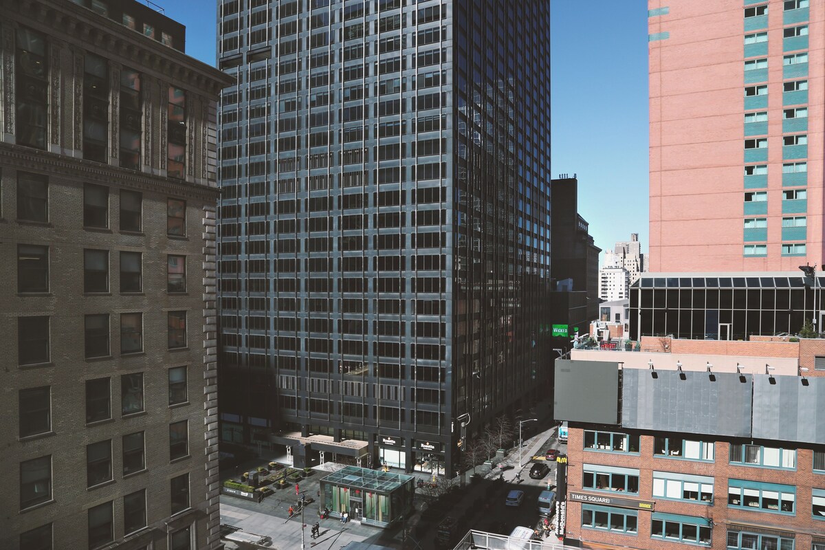 A high-rise building with a grid of windows, adjacent older brick buildings, and a clear sky.