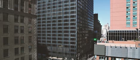 A high-rise building with a grid of windows, adjacent older brick buildings, and a clear sky.