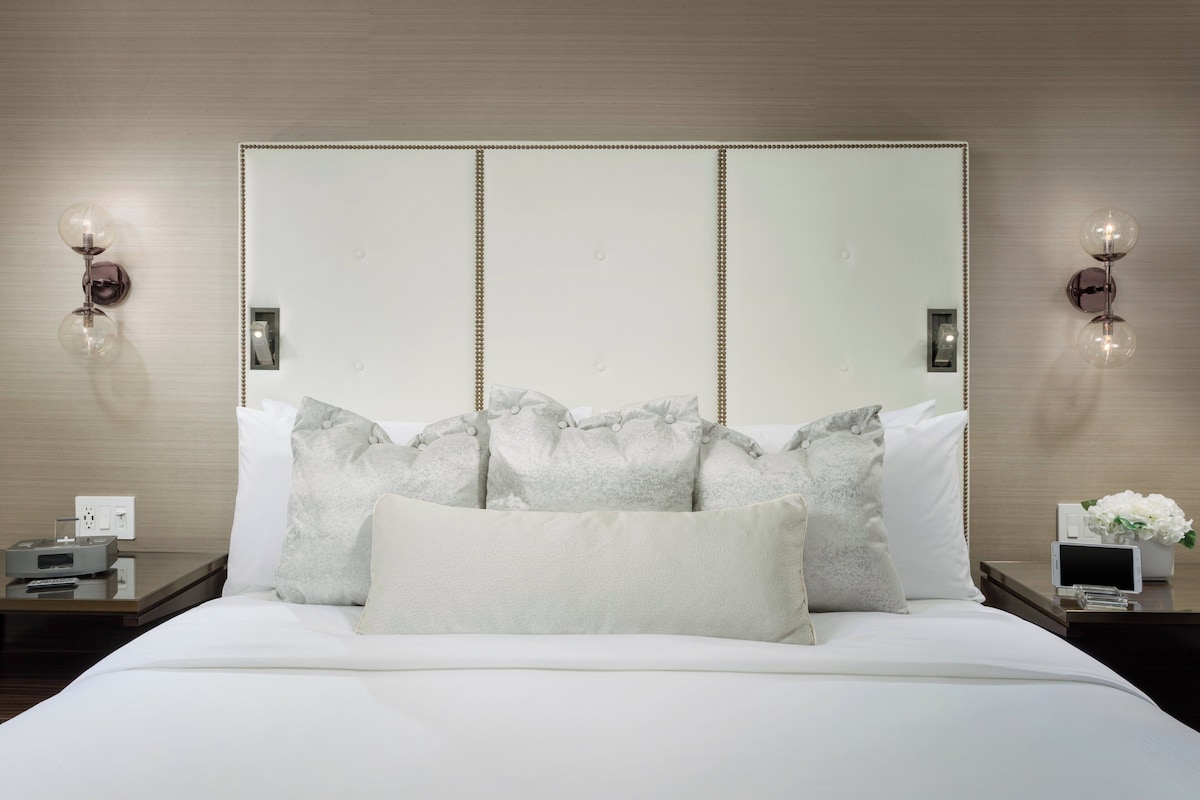 A neatly made bed with a large mirror above it, flanked by two bedside tables with lamps and a small clock.
