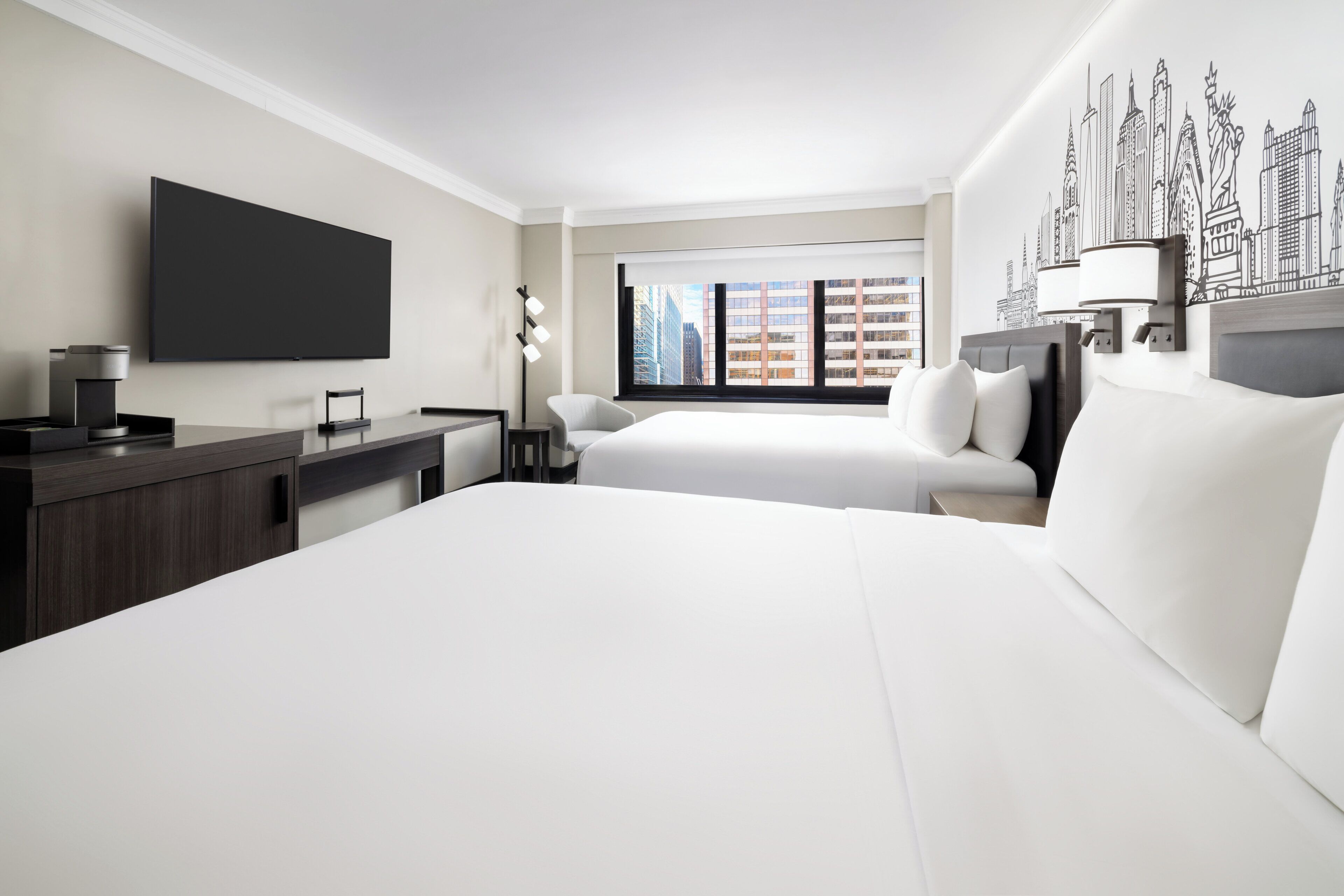 Una moderna camera d'albergo con un letto grande, una scrivania, una TV a schermo piatto e un murale con una veduta sulla città.