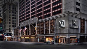 A hotel with a prominent 'M' logo, 'The Manhattan at Times Square Hotel' signage, and 'An American Craftsman' storefronts.