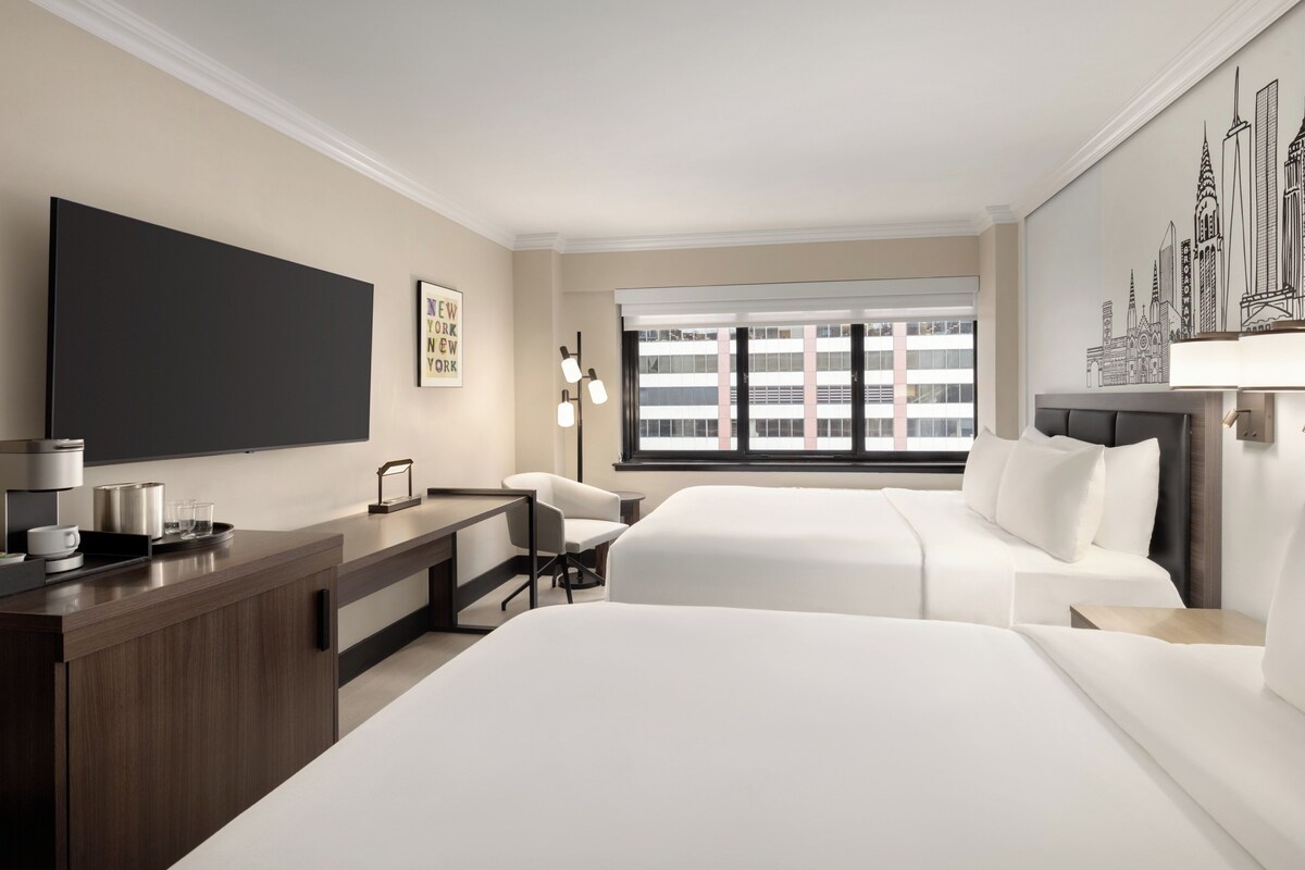 Une chambre d’hôtel dotée d’un grand lit, d’un bureau avec une machine à café, d’une télévision à écran plat et d’une fenêtre offrant une vue sur le paysage urbain.