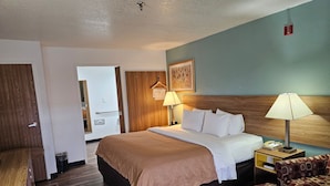 A hotel room with a bed, bedside lamps, a wooden headboard, a wooden floor, and a patterned sofa.