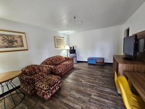 A living room with a patterned sofa, a small table, a TV, and a blue cabinet. - Days Inn by Wyndham Blythe (Blythe)