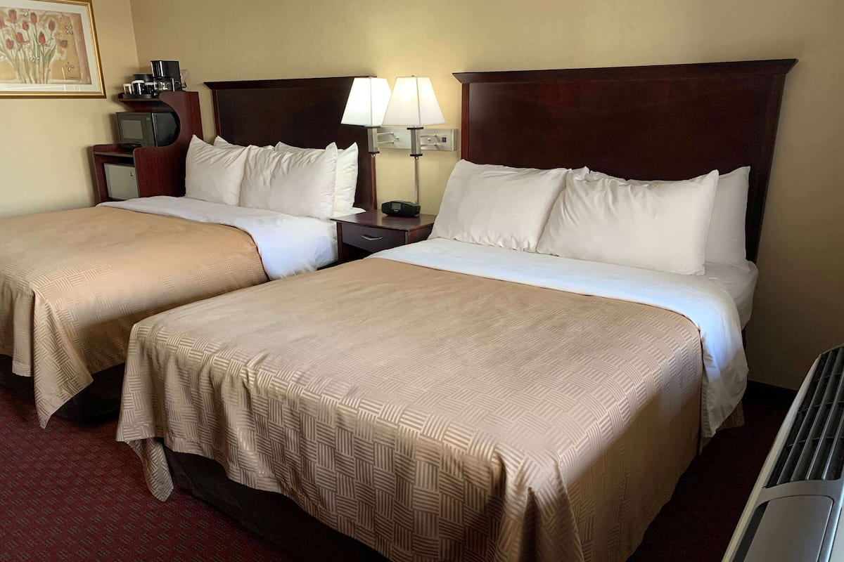 A hotel room with two beds, a desk, a lamp, a television, and a coffee maker.