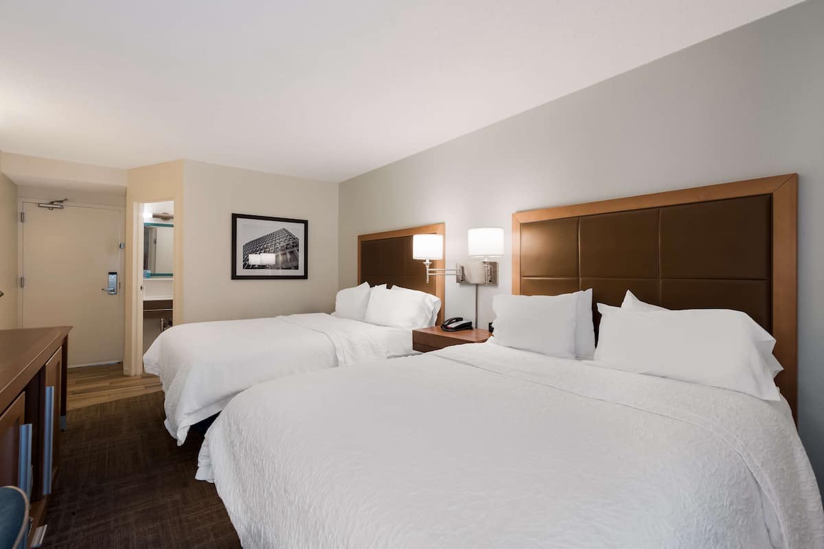 A hotel room with two beds, a desk, and a bathroom visible through an open door.