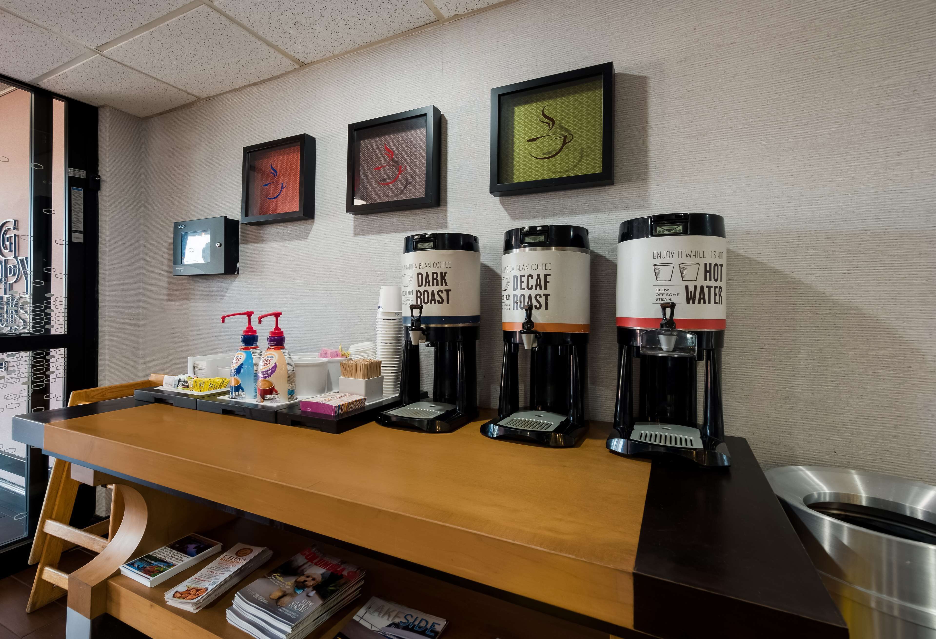 A coffee station with four coffee dispensers labeled 'Dark Roast' and 'Decaf Roast', and a 'Hot Water' dispenser. There are also condiments and napkins on the counter.