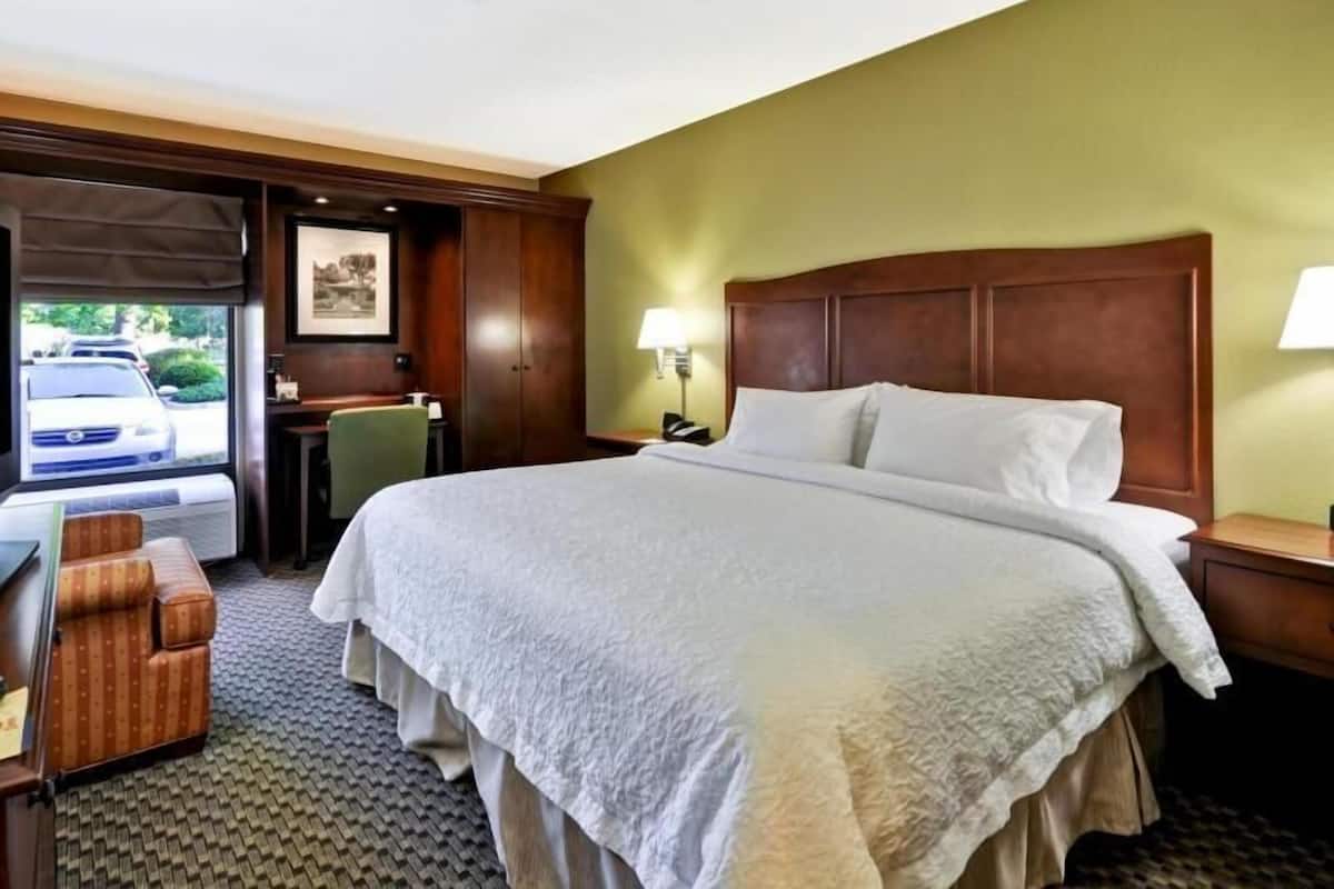 A hotel room with a large bed, a desk, a chair, and a view of a parked car outside.