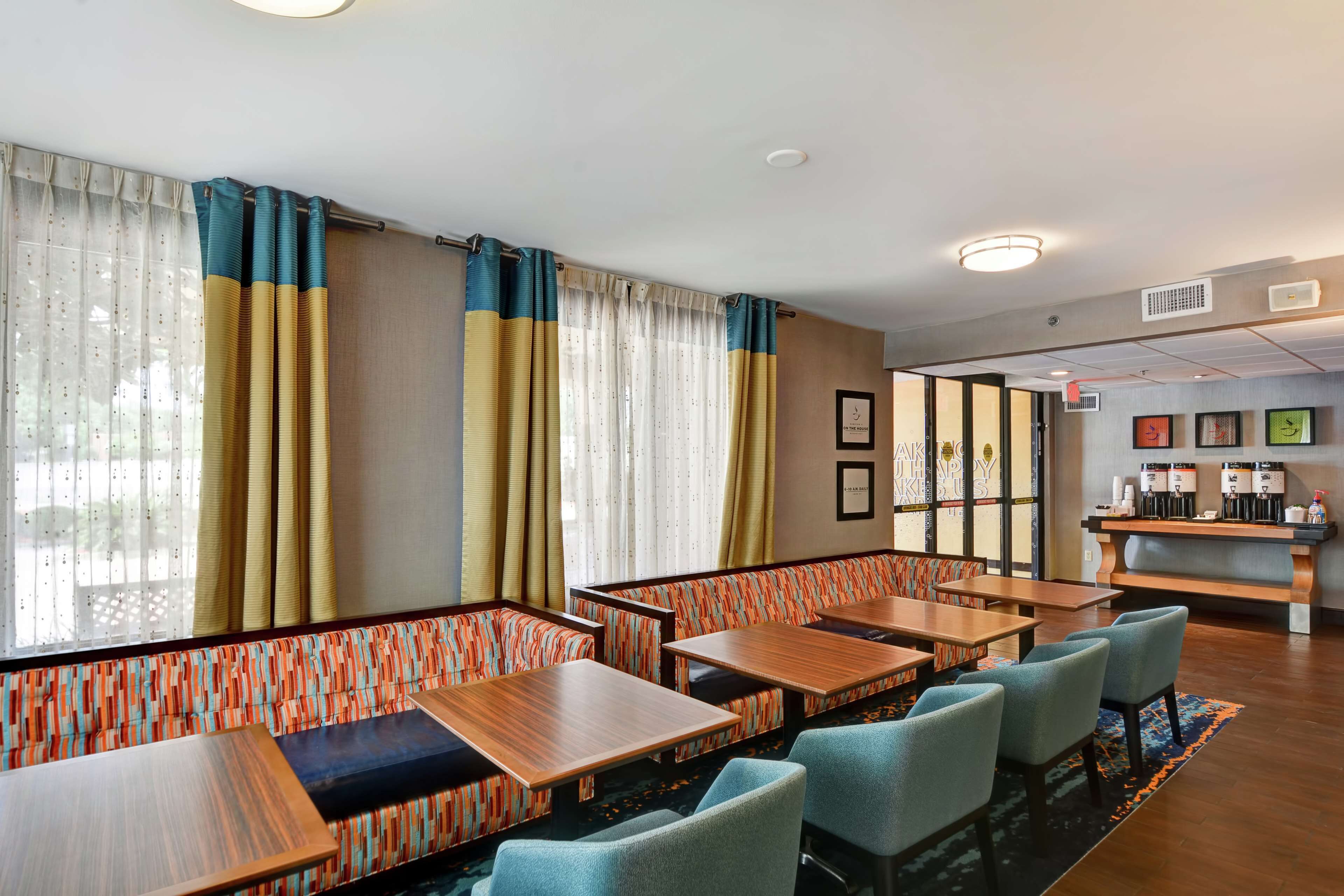 A hotel room with a dining area featuring wooden tables and cushioned seating.