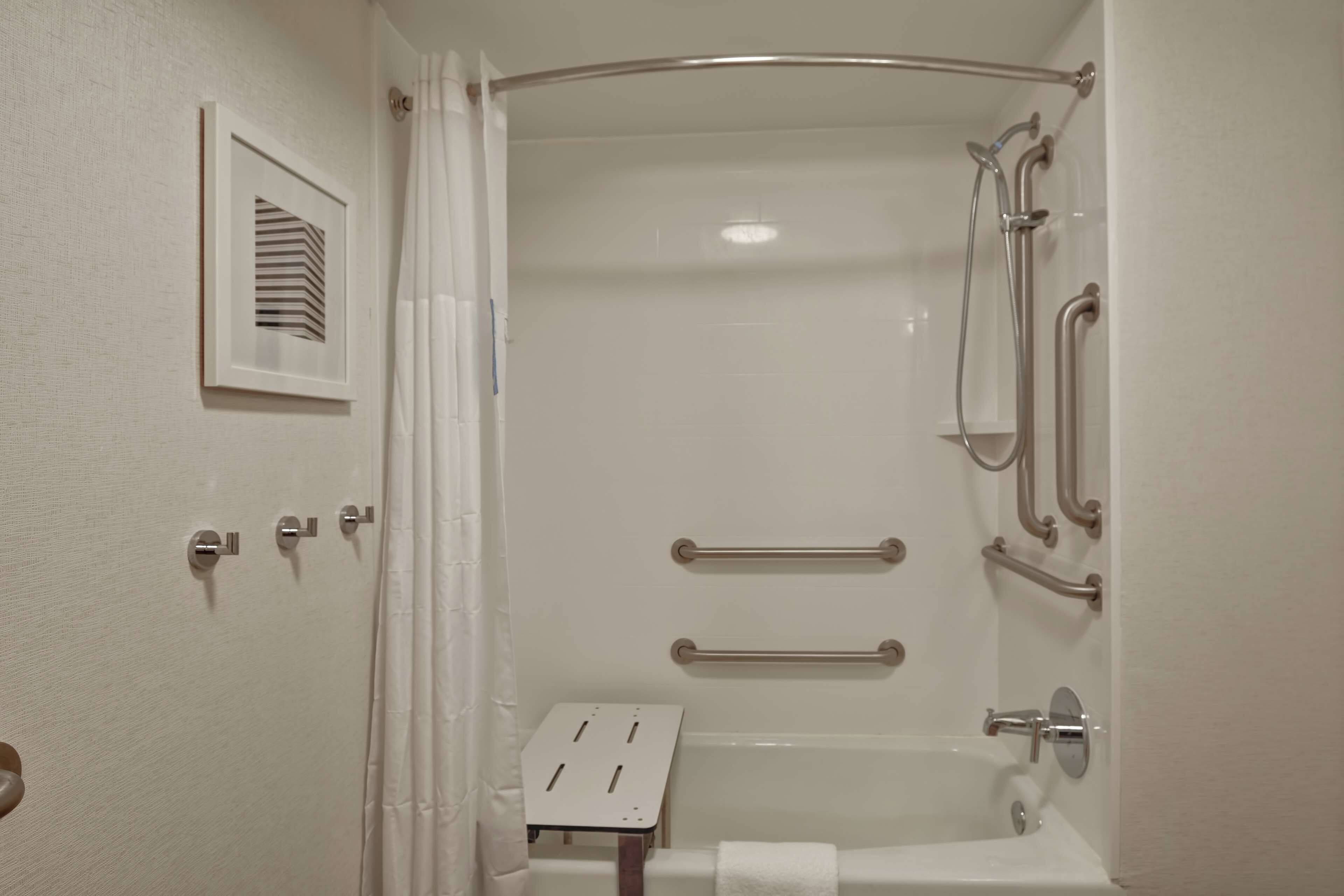 A bathroom with a bathtub, a shower, and a toilet. There are grab bars and a towel rack.