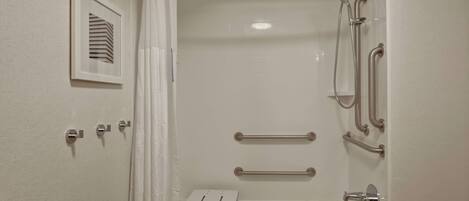 A bathroom with a bathtub, a shower, and a toilet. There are grab bars and a towel rack.